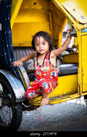 A cute Filipino girl plays on her fathers tricycle, pedicab or rickshaw in Ermita, Manila, Philippines. Stock Photo