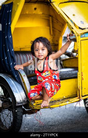 A cute Filipino girl plays on her fathers tricycle, pedicab or rickshaw in Ermita, Manila, Philippines. Stock Photo