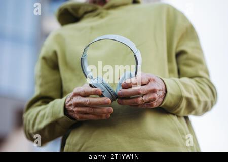 Close up of elderly man holding wireless headphones, listening music while exercising outdoors. Stock Photo