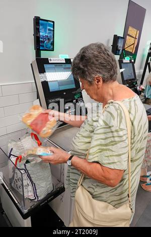 M&S interior foodhall scan & pay checkout till mature senior woman passing food item over bar scanner & security face camera screen on wall England UK Stock Photo