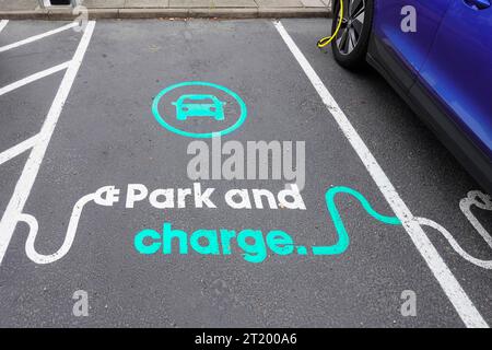 Close up view park and charge graphic painted on tarmac surface of car parking bay reserved for electric cars to top up at Holiday Inn Hotel Essex UK Stock Photo