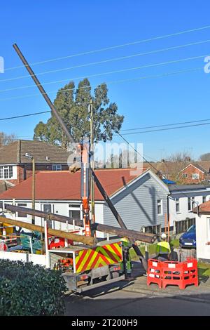 Electrical engineering contractors install new timber pole to carry replacement overhead electricity cables to houses in residential road England UK Stock Photo