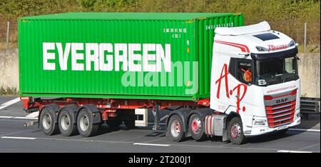 EVERGREEN brand of shipping container on semi trailer towed by haulage business white DAF prime mover hgv lorry truck driving on M25 UK motorway road Stock Photo