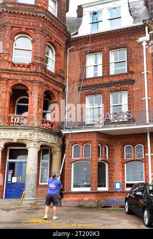 Window cleaner workman operating an extendable water fed light weight pole to reach glazing on third floor windows at Hotel de Paris Cromer Norfolk UK Stock Photo