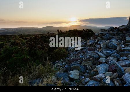 Standing by the side of the cairn on Llanbedrog Headland as the summer sun sets over Eryri National Park. Stock Photo