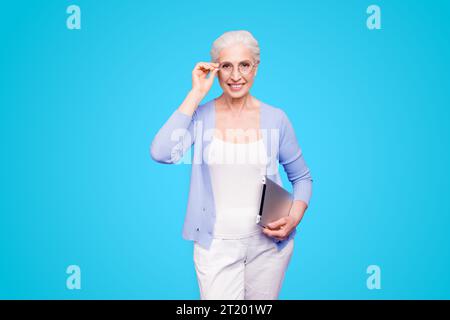 Grey haired old smiling business woman wearing glasses, holding tablet. Isolated over violet purple background Stock Photo