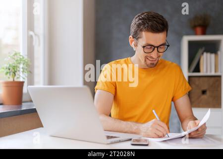 Smiling guy student wearing wireless headphone study online with skype teacher, has online class. Happy young man learn language, listen lecture, watch webinar, write notes. Distant education concept Stock Photo