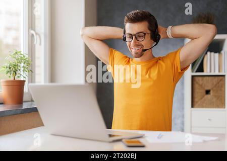 Young happy man sitting at home office,smiling, enjoying work or study remotely from home by Internet, video call or online conference on laptop. Student freelancer resting during remote work process Stock Photo