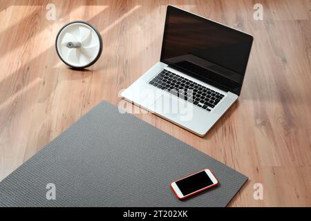 Closeup of equipment for online fitness at home: exercise mat, smartphone, laptop, health progress app. Workout or yoga online while quarantine and self isolation. Copy space Stock Photo