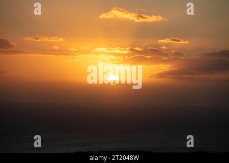 Sunset through and behind the cloudscape over the sea background. Sunbeam colors orange the sky, golden sun hides behind strange shaped cloud Stock Photo