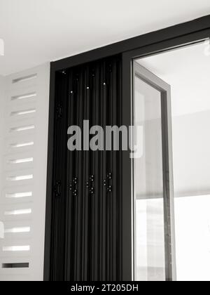 Close-up door hinges on the black aluminum folding doors with glass on white building background, vertical style. Stock Photo