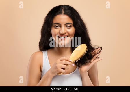 Beauty Routine. Attractive happy indian woman brushing her curly hair with comb Stock Photo