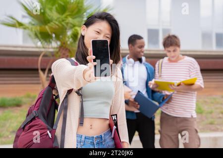 Young smiling Asian student holding and showing empty screen of smartphone Stock Photo