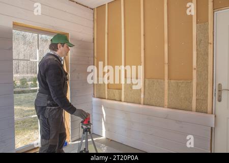 The worker makes finishing works of walls with a white wooden board, using laser line level. Stock Photo