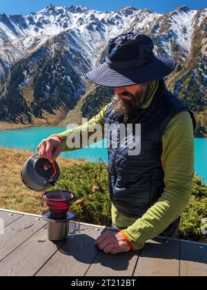 Bearded male tourist preparing coffee while camping high in the mountains. Hiking in the highlands. Preparing breakfast while traveling Stock Photo
