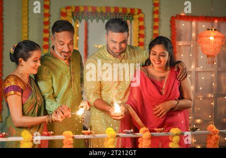 happy Senior parents with son and daughter in law celebrating Diwali festival by playing with sparklers or fireworks - concept of family reunion Stock Photo