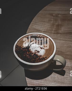 A white ceramic cup with a handle sits on a wooden table with a backdrop of brown and white paint Stock Photo