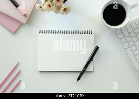 White office desk table with blank notebook, computer keyboard and other office supplies. Top view with copy space, flat lay.. Stock Photo