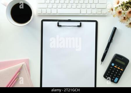White office desk table with blank notebook, computer keyboard and other office supplies. Top view with copy space, flat lay.. Stock Photo