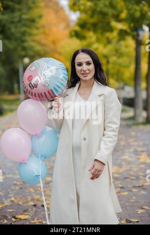 Beautiful pregnant woman holding blue and pink inflatable balloons. Inflatable balloons that allow you to find out the gender of your unborn child. Ge Stock Photo