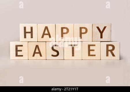 The Word HAPPY EASTER on wooden cubes on a beige neutral studio background. Copy Space. Written. Text words matter. Inscription Happy Easter. Greeting Stock Photo