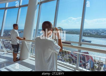 Samut Prakan, Thailand - September 3, 2023: a boy looks at Chao Phraya River's shores through binoculars at observation deck of Samut Prakan Tower Stock Photo