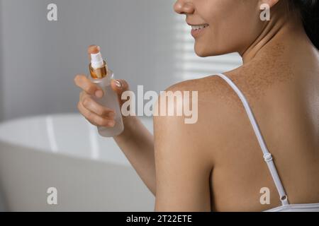 Young woman holding bottle of body oil in bathroom, closeup. Space for text Stock Photo