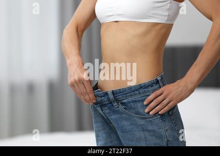 Slim woman wearing big jeans at home, closeup. Weight loss Stock Photo