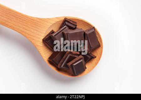 Broken bitter dark chocolate bar with pieces in wooden spoon on white ceramic dish close up. Sweet baking ingredient Stock Photo