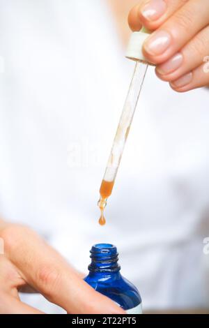 A close side shot of a blue bottle with serum, drops falling from a pipette. Close up shot of drops of moisturizing serum for skin. A product for midd Stock Photo