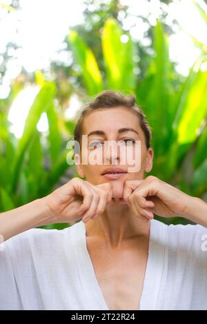 Vertical portrait of a middle-aged woman doing a facial massage and smiling. Self-facial massage and daily skin care in adulthood. Organic cosmetics f Stock Photo
