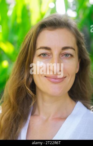 Close-up shot of a beautiful middle-age woman's face applying moisturizing and nourishing cream to her face, look at camera and smile. Facial skin car Stock Photo