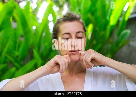 Close up photo of a middle-aged woman doing a facial massage using massage cream. Daily skin care and fight against age-related changes. Facial skin c Stock Photo