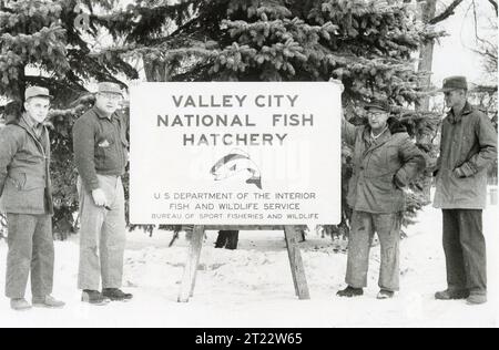 Fish and Wildlife Service staff members stand beside a hatchery identification sign, representing agency operations and facilities in the Central Plains Region. Stock Photo