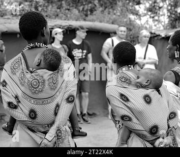 Tribal women of Maasai Mara wearing their traditional dress carrying their kids and entertaining the visitors in their village Stock Photo