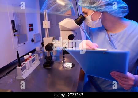 Female scientist taking notes during microscopic examination of cell samples Stock Photo