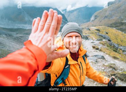 Smiling backpacker dressed orange jacket giving High Five to female mate during Himalaya valley trekking. Mera peak climbing route near the Khare sett Stock Photo