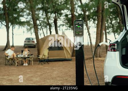 Alternative family vacation trip traveling by the beach with electric car recharging battery from EV charging station with two family kid enjoying the Stock Photo