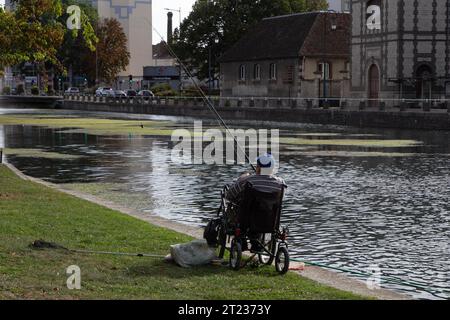 A fisherman in a wheelchair waits for the fish to bite on the Canal du Trévois in Troyes city centre, France. Stock Photo