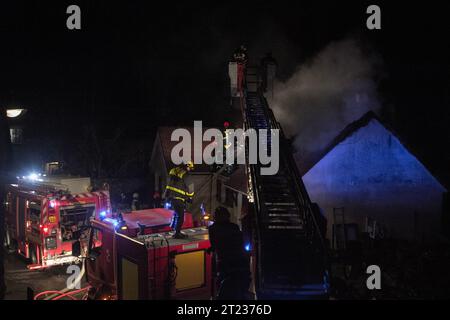 Firemen fight a house fire in a village in France at night with two fire engines and an extendable ladder. Stock Photo