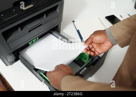 Close-up of hands of young male white collar worker preparing for copying documents while putting stack of paper in xerox tray Stock Photo