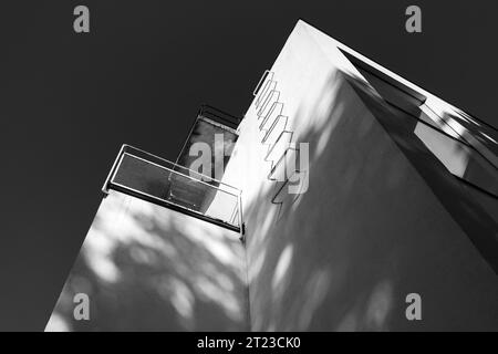 Corner of white walls with metal stairs under dark sky, fire escape way. Abstract architecture background. Black and white photo Stock Photo
