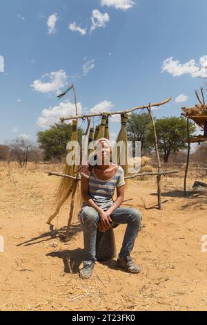 entrepreneur african woman in the village , sited on a bucket, selling brooms on the side of the highway to the truckers passing by Stock Photo