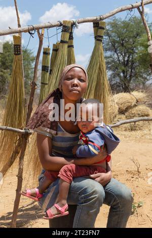 african woman in the village , holding her baby in the lap, selling brooms as a street vendor near the highway Stock Photo