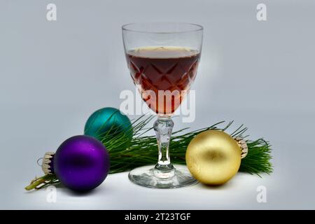 Three colored Christmas baubles and a sprig of spruce Christmas tree and a glass of port wine in studio shot with white background Stock Photo