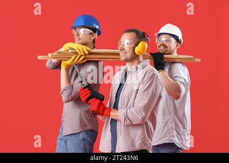 Team of male builders with wooden planks on red background Stock Photo