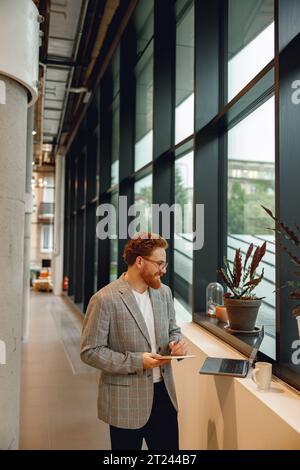 Handsome businessman working on project while using laptop and making notes while standing in office Stock Photo