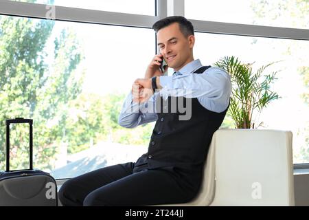 Handsome steward talking by mobile phone in hall of airport Stock Photo