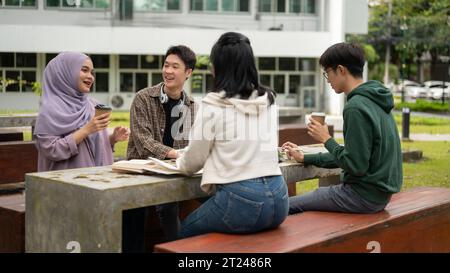 A group of diverse young college students is discussing and working on a group project at a table in a campus park together. Education concept Stock Photo