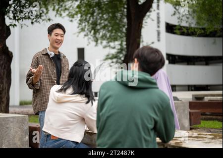 A cheerful and smart young Asian male college student is tutoring math to his friends in a campus park. Education concept Stock Photo